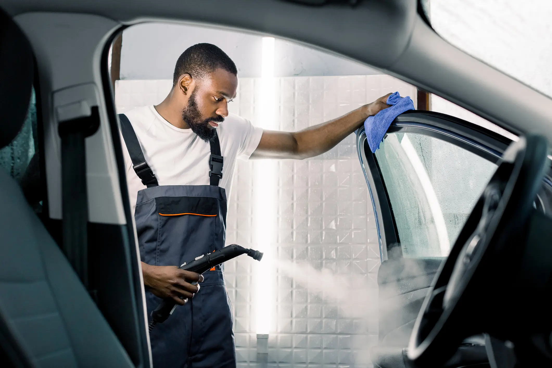 Man steam cleaning car interior with cloth.