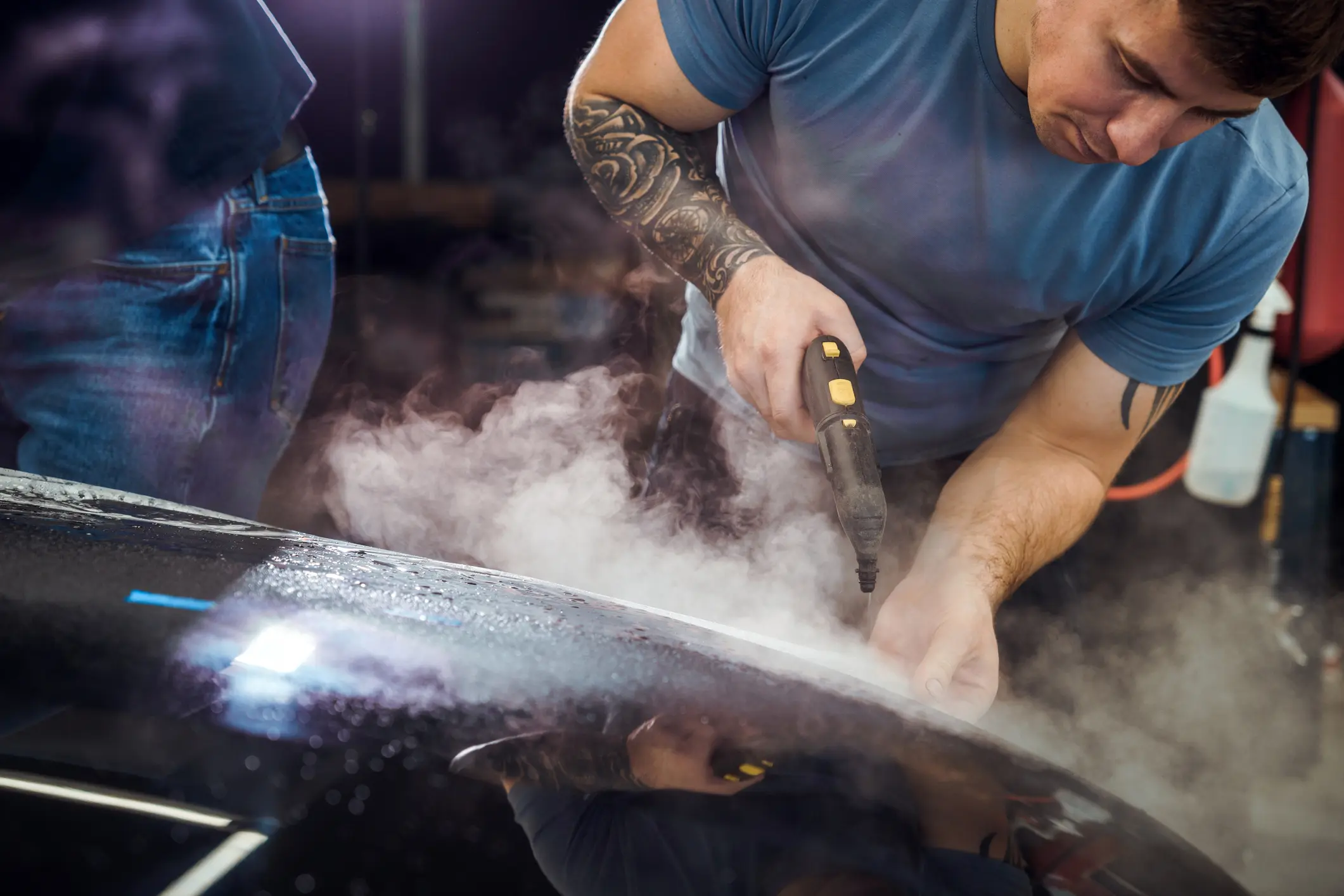 Man steam cleaning a car exterior surface.