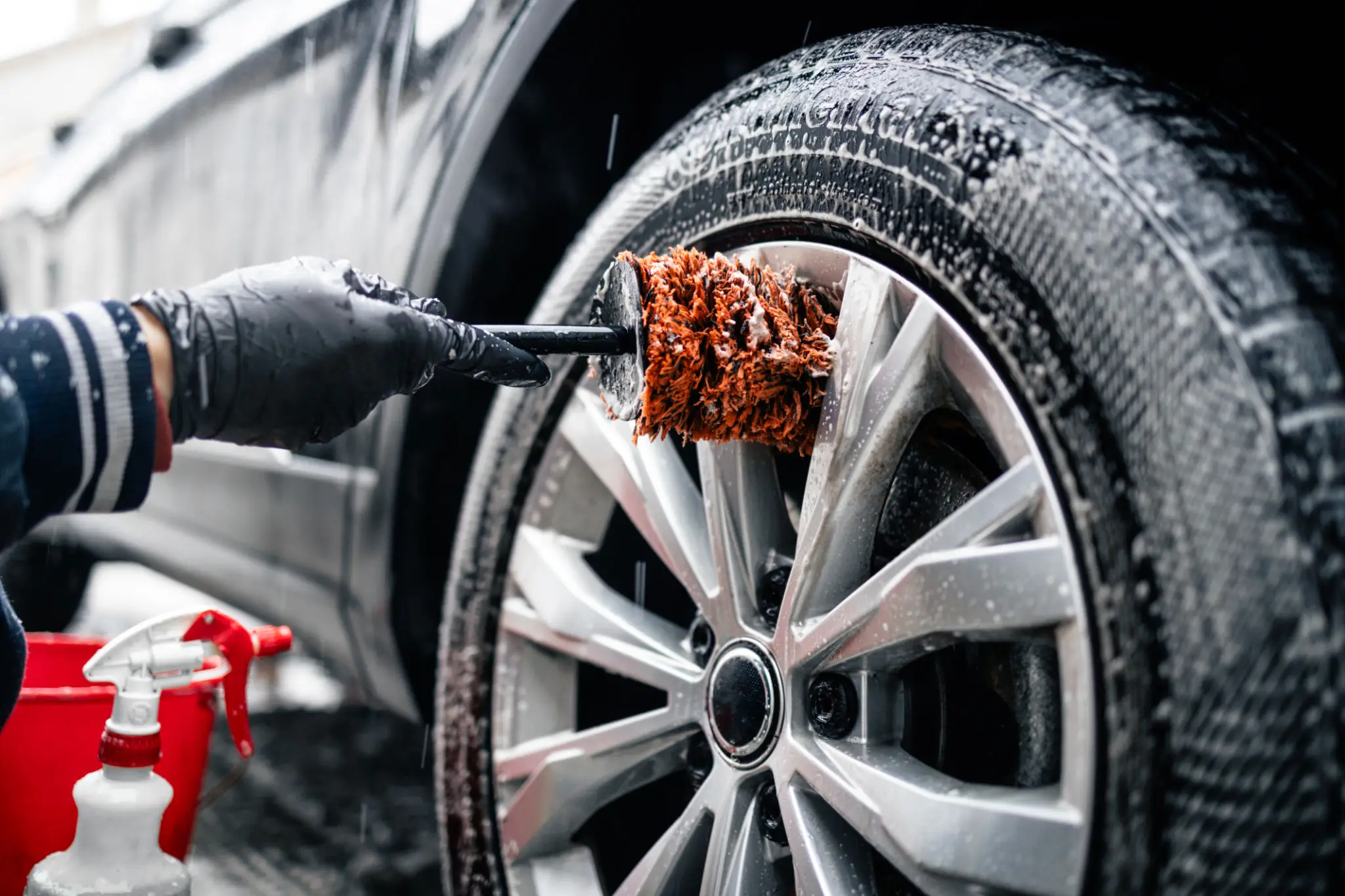 Cleaning car wheel with brush and spray.