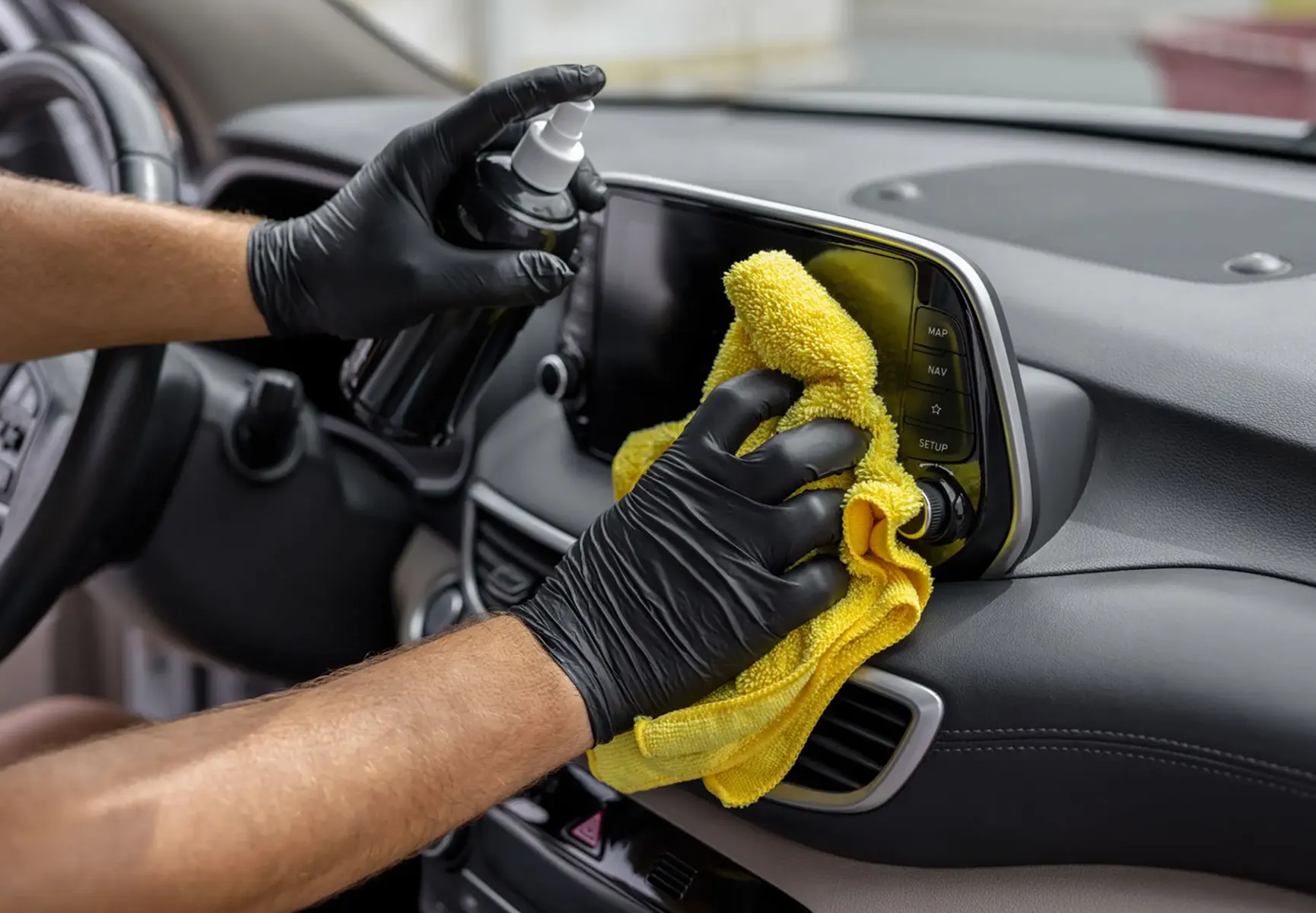 Cleaning car dashboard with spray and cloth.